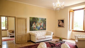 A living room with a white sofa, a red rug, a chandelier, and a painting on the wall. - Agriturismo il Casolare - Villa Vettori (Poppi)