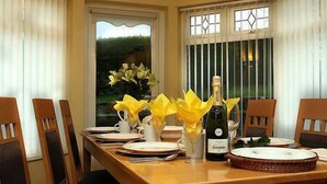 A dining table set with plates, a bottle, and a vase with yellow flowers. - Crockgarve (Dungannon)