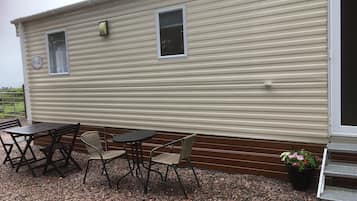 A mobile home with a patio area featuring a table and chairs, a small window, and a door.