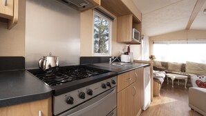 A compact kitchen with a stove, oven, and microwave, wooden cabinets, and a window providing natural light. - Crockgarve (Dungannon)