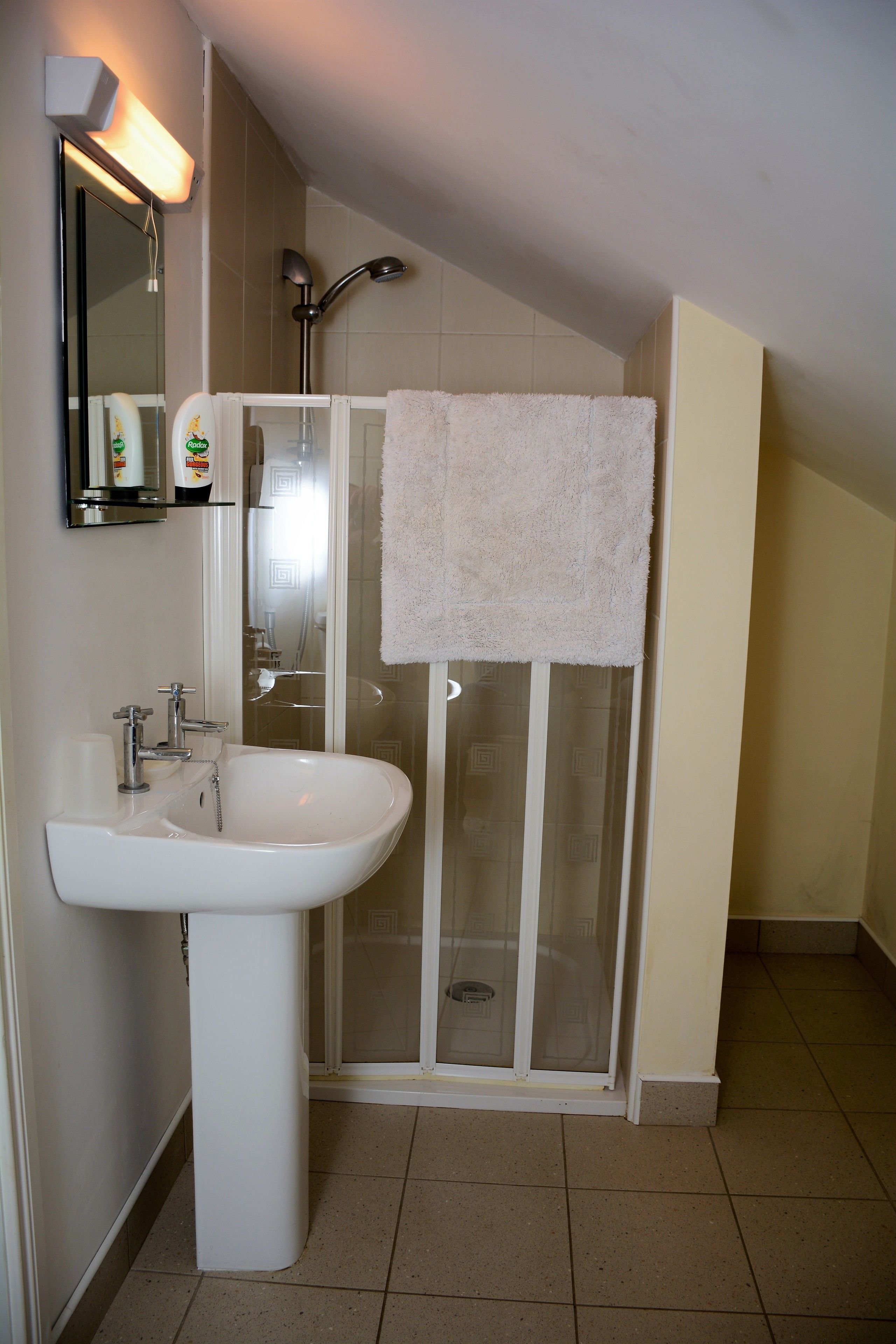 Un baño con lavamanos blanco, cabina de ducha de vidrio y una toalla colgada en la puerta de la ducha.