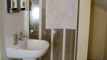 Un baño con lavamanos blanco, cabina de ducha de vidrio y una toalla colgada en la puerta de la ducha.