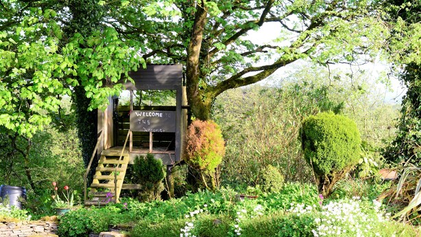 A wooden structure with a sign reading "WELCOME TO THE GARDEN" surrounded by lush greenery and a stone wall. - Crockgarve (Dungannon)
