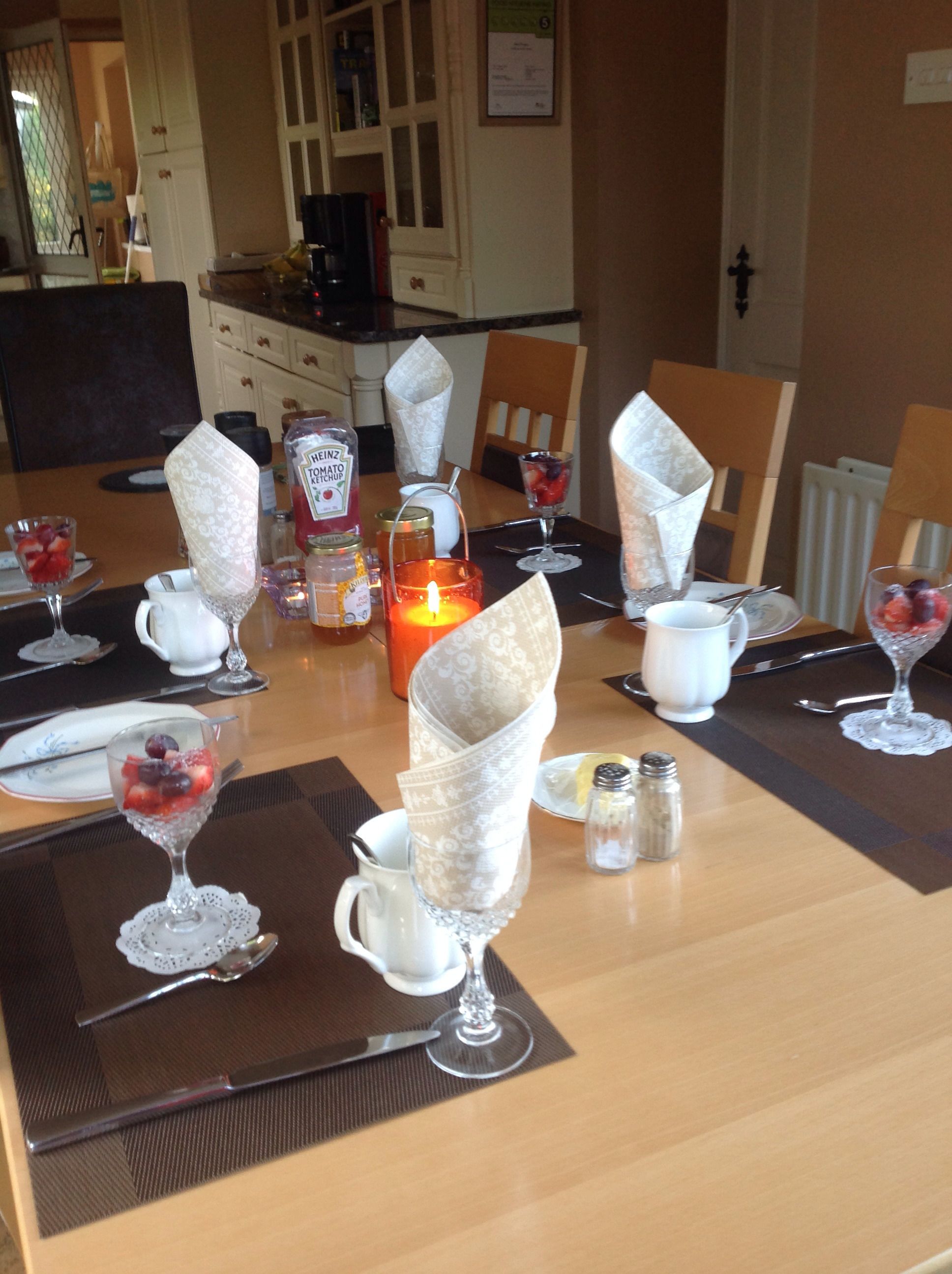 A dining table set with white napkins, clear glassware, and a lit candle.