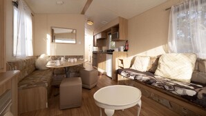 A compact RV interior with a kitchenette, a dining area, and a seating area with a sofa and ottoman. - Crockgarve (Dungannon)