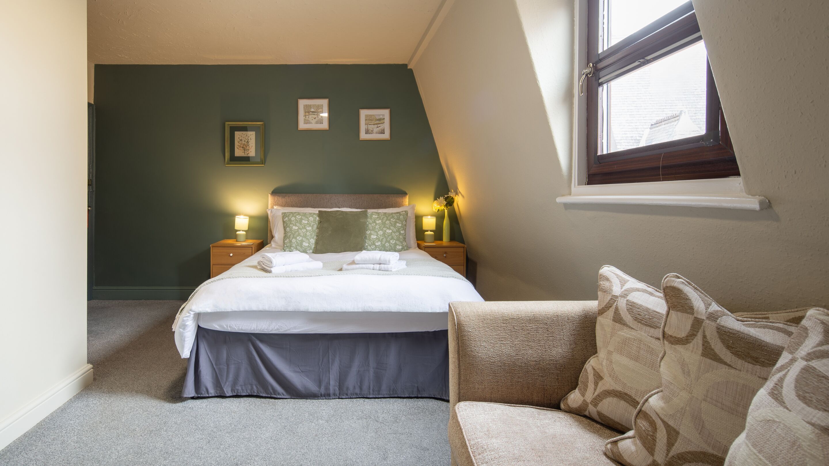 A bedroom with a bed, bedside tables, a window, and a view of the outside.