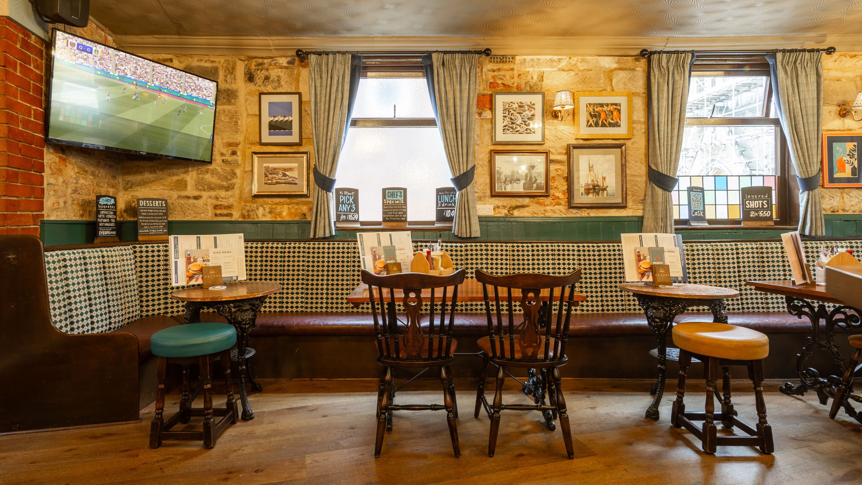 A pub with a stone wall, wooden furniture, and a TV screen displaying a sports game.