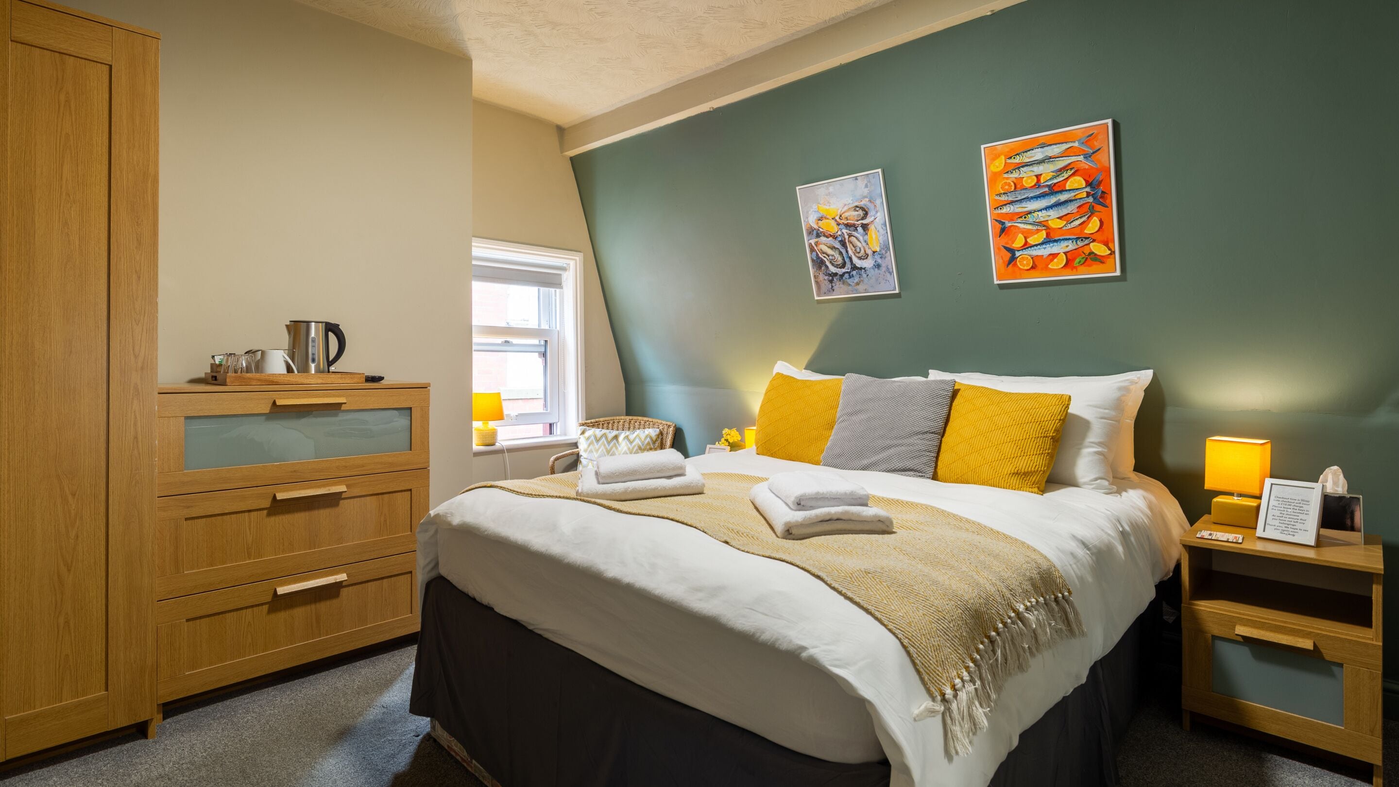 A bedroom with a bed, wooden dresser, bedside tables, and artwork on the wall.