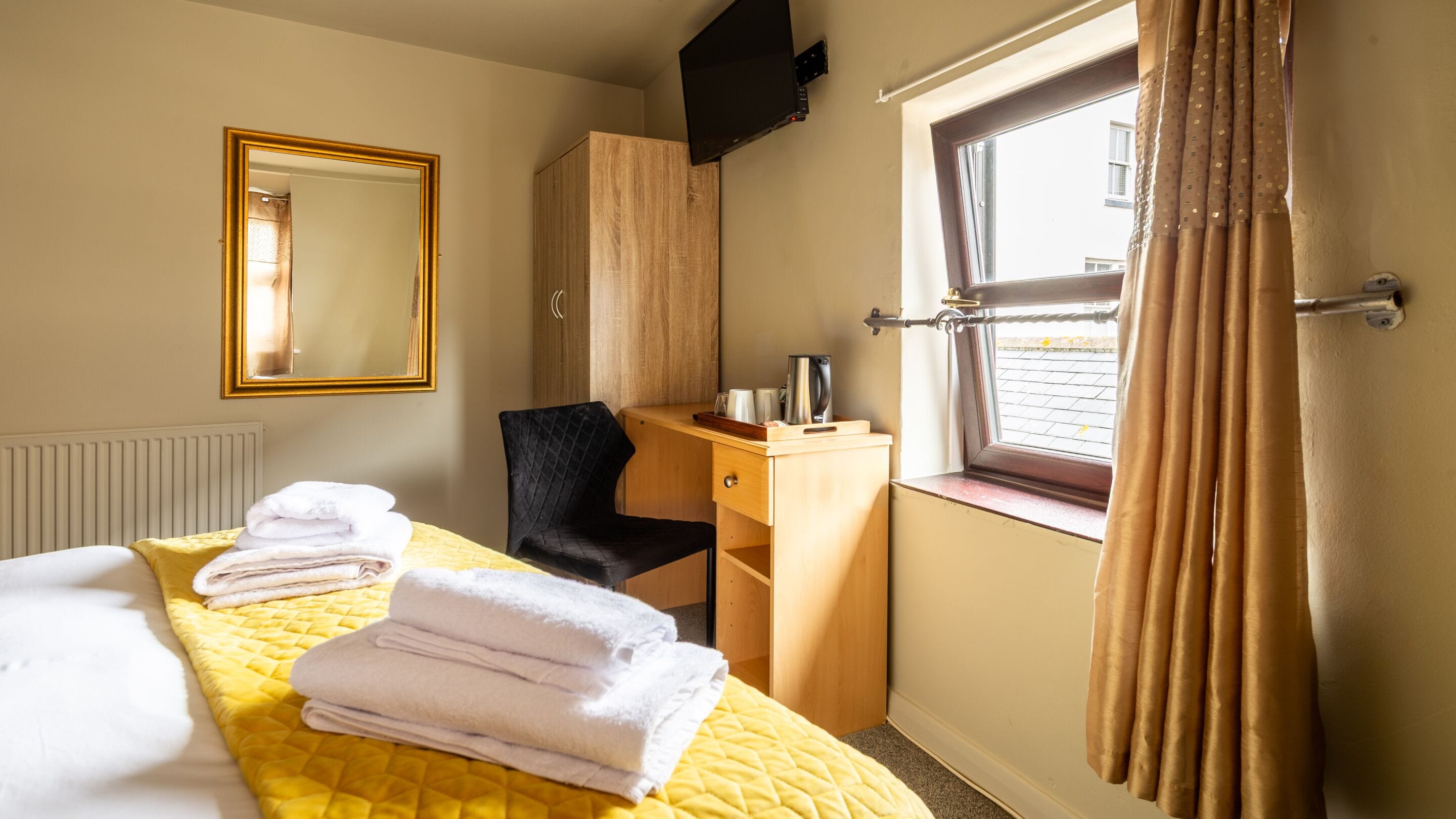 Una habitación de hotel con cama, escritorio, silla, televisor y ventana con cortinas.