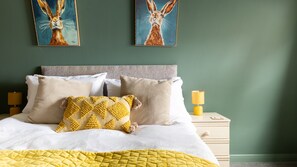 Un lit recouvert d’une couette blanche et jaune, agrémenté de plusieurs oreillers, et deux tableaux représentant des lapins accrochés au mur.