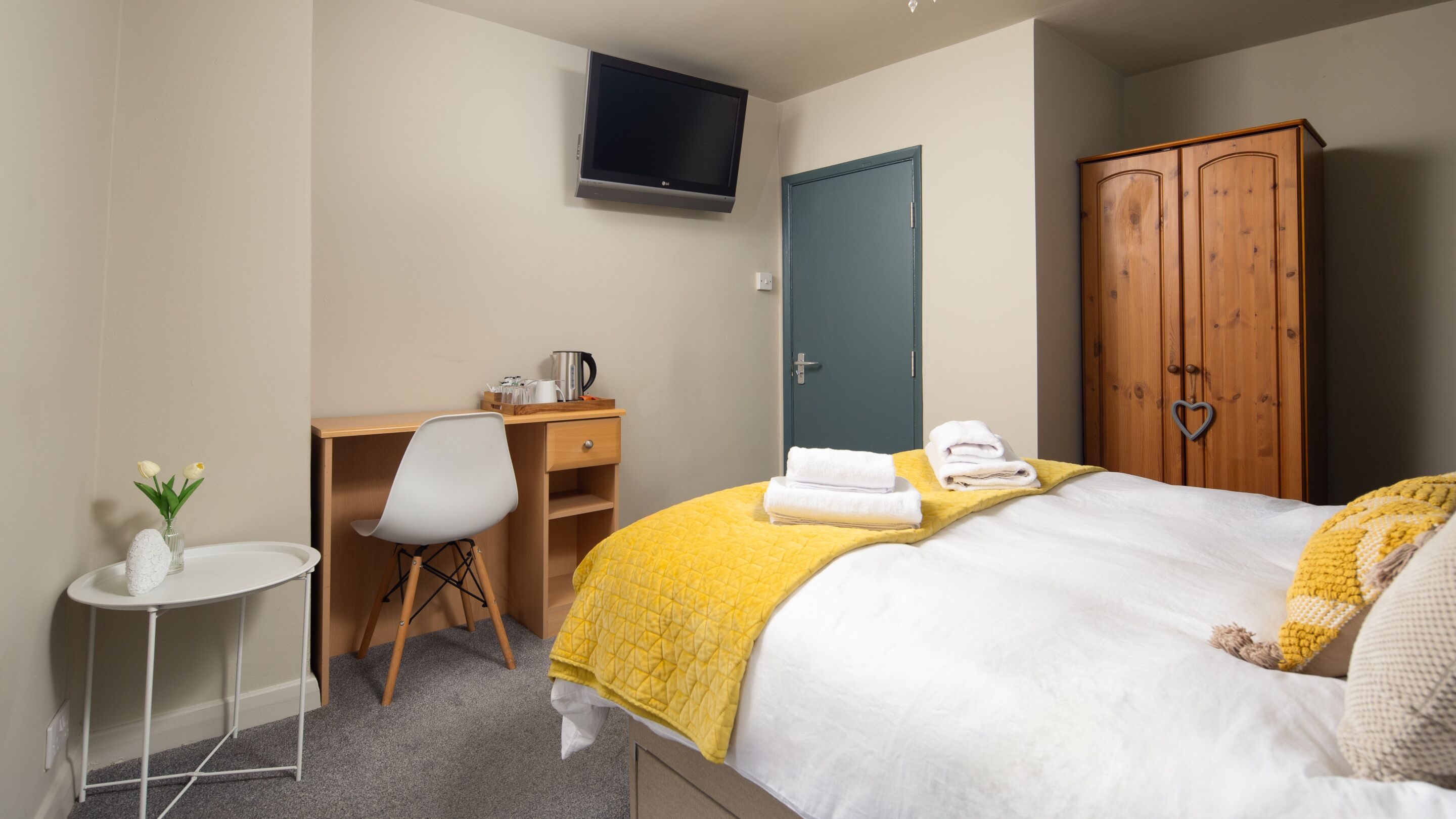 Habitación de hotel con cama, escritorio, silla, televisor, armario y una pequeña mesa con un florero.