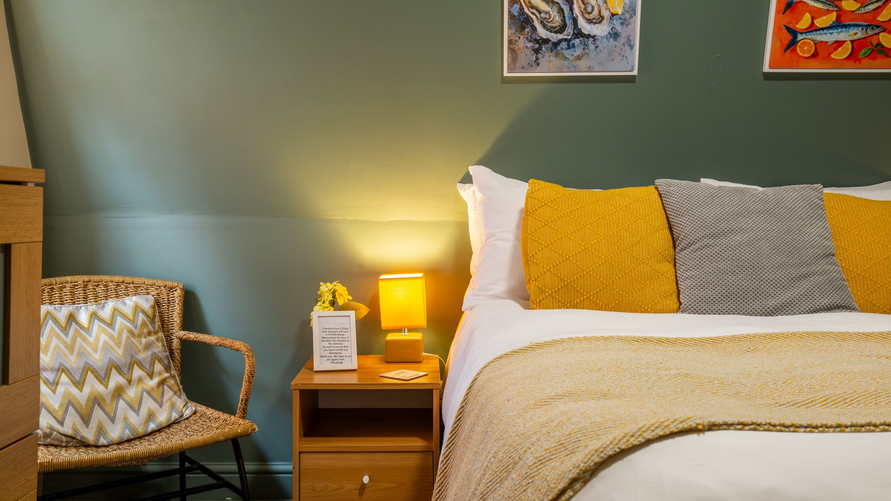 A neatly arranged hotel room with a bed, a chair, a nightstand with a lamp, and artwork on the walls.
