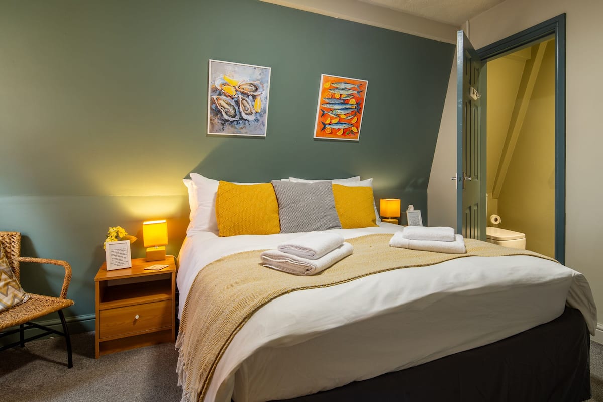 Een hotelkamer met een bed, nachtkastje, stoel, spiegel en kunst aan de muur.
