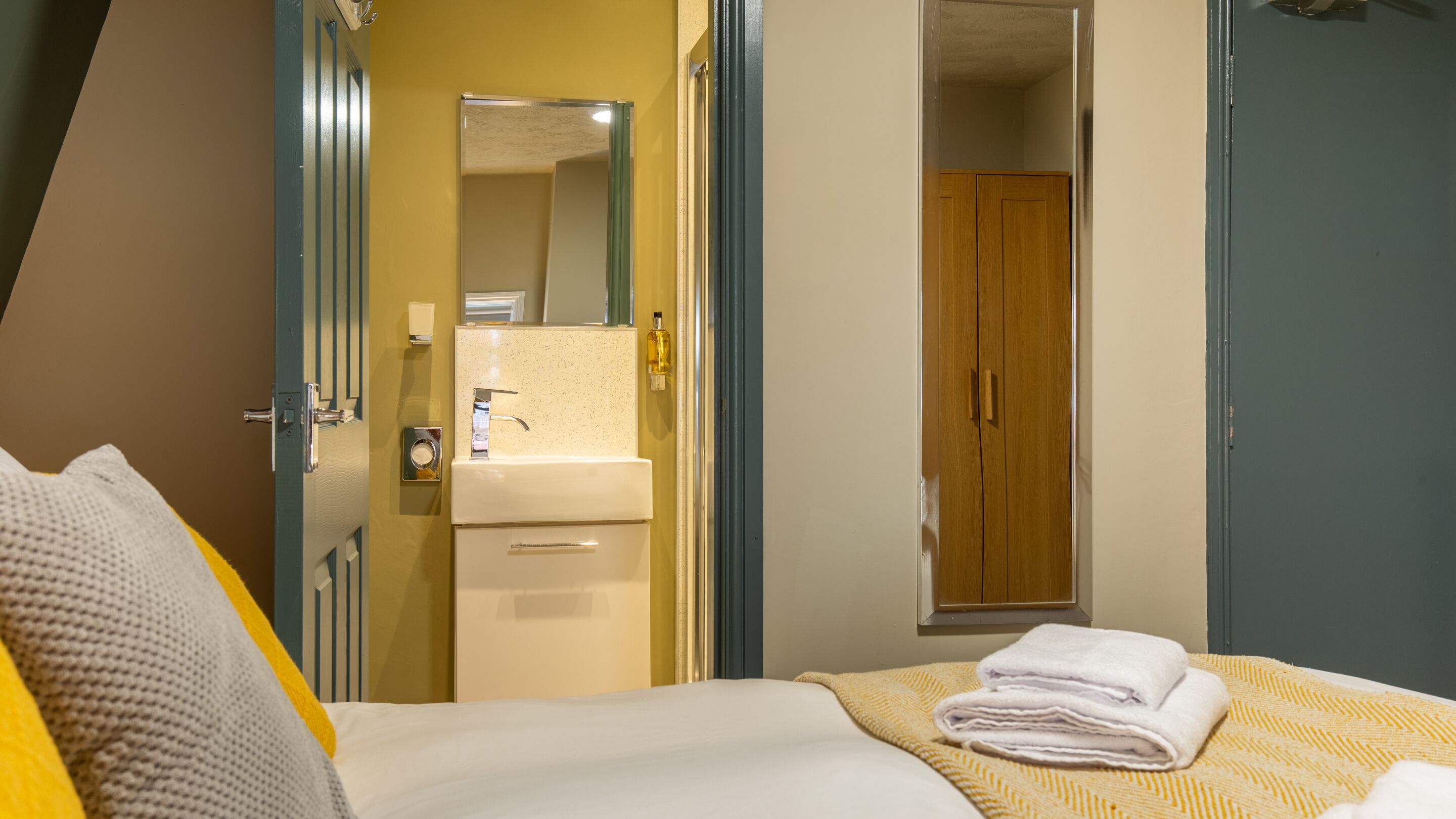 Une chambre d’hôtel comprenant un lit, une salle de bain avec un lavabo et un miroir, et une armoire en bois.