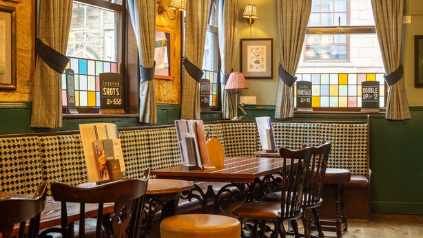 A cozy pub with wooden furniture, a menu board, and a window with a view of the street.