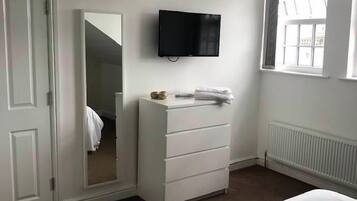 Ein Schlafzimmer mit einem Bett, einem Schminktisch, einem Spiegel, einem Fernseher und einem Fenster.