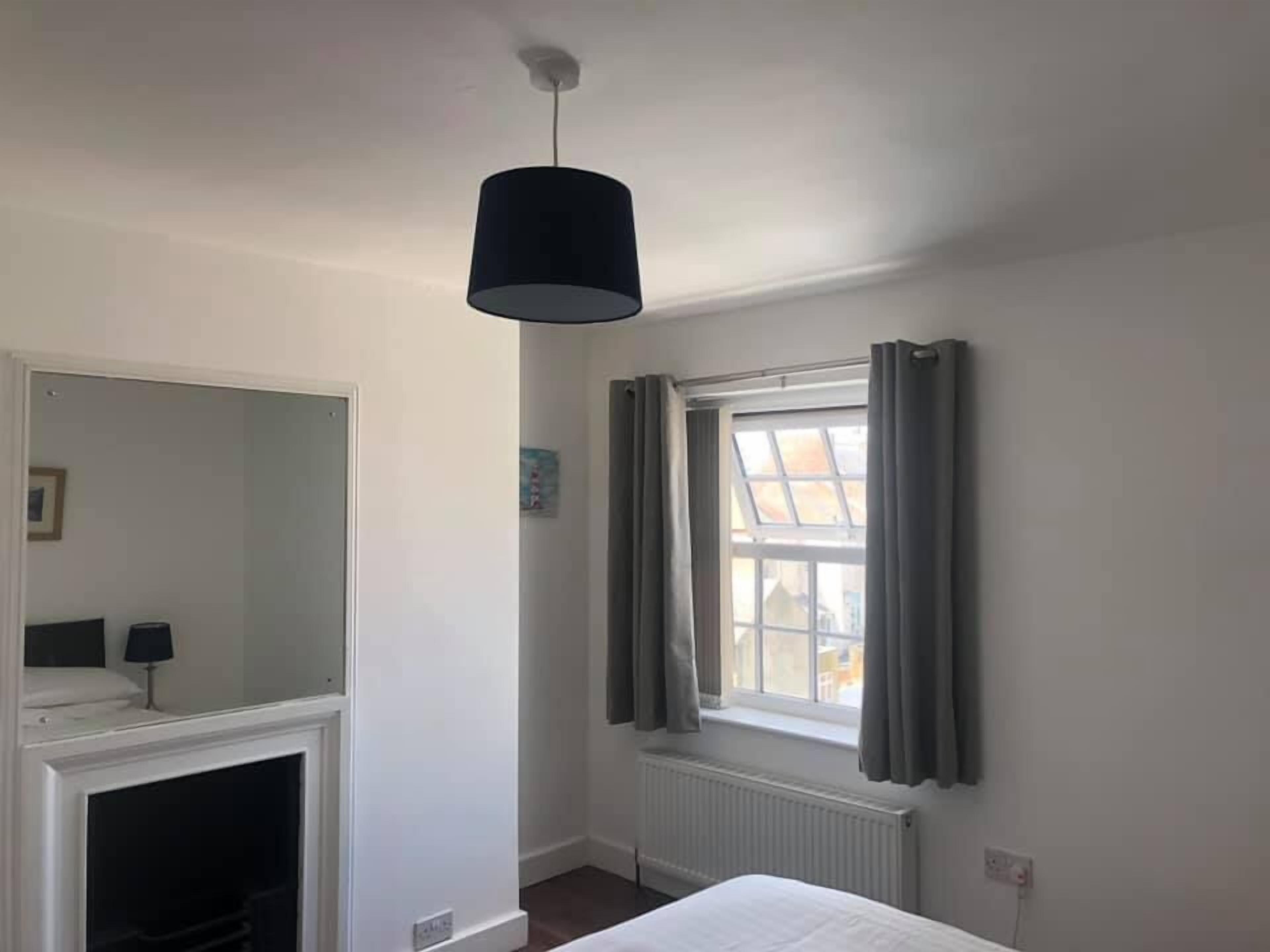 Una camera da letto con un letto, una finestra con tende, un termosifone e una lampada a sospensione.