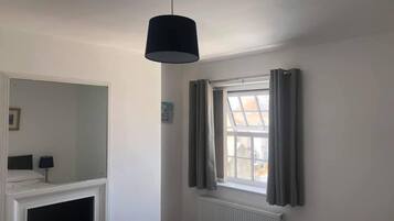 A bedroom with a bed, a window with curtains, a radiator, and a hanging light fixture.