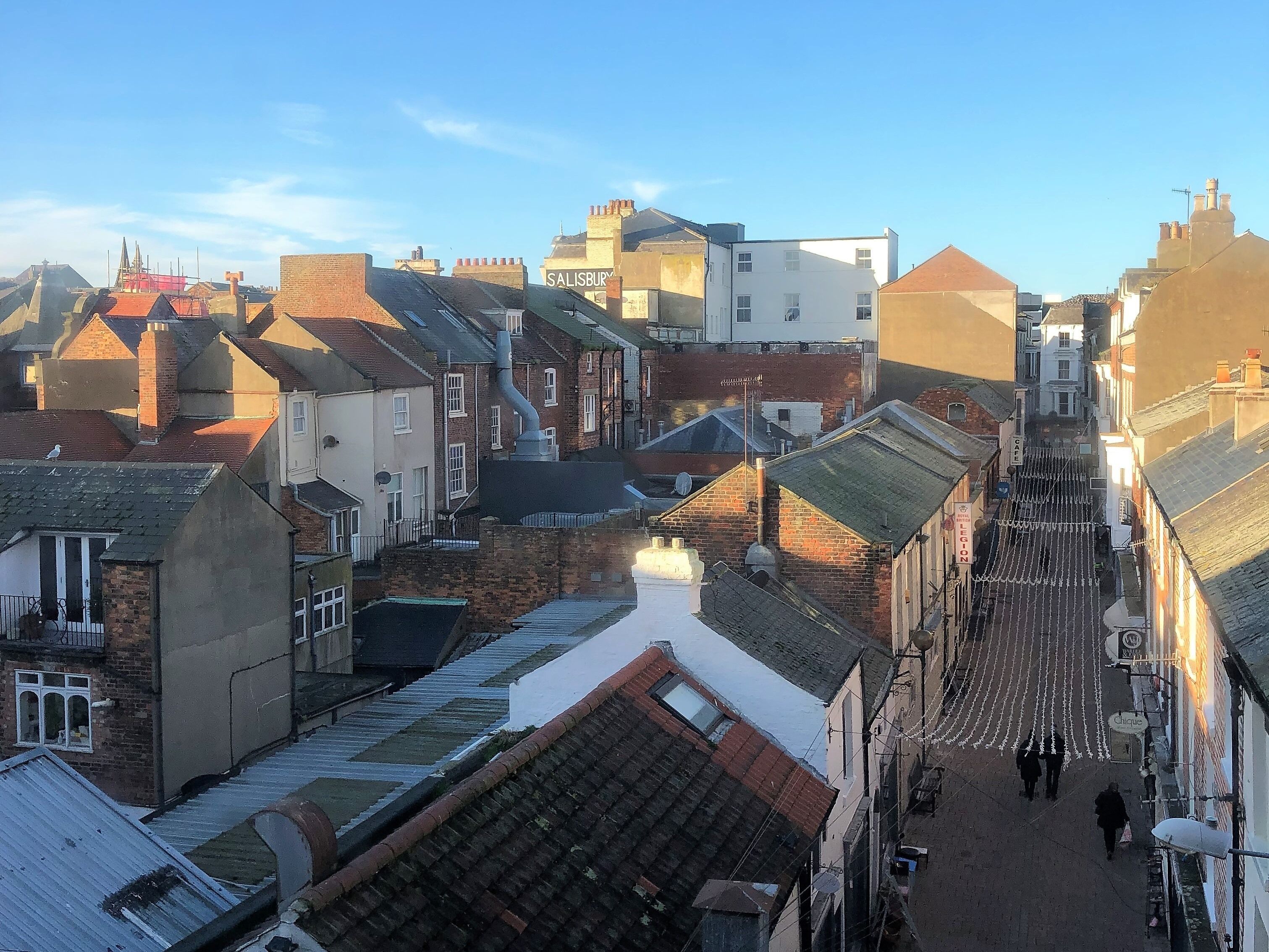 Une rue étroite bordée de bâtiments traditionnels, dont certains présentent des cheminées apparentes et des toits en tuiles.