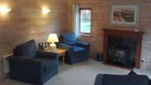 A cozy room with wooden walls, a fireplace, and two blue armchairs. - The Log Cabin Glebe Farm (Market Rasen)