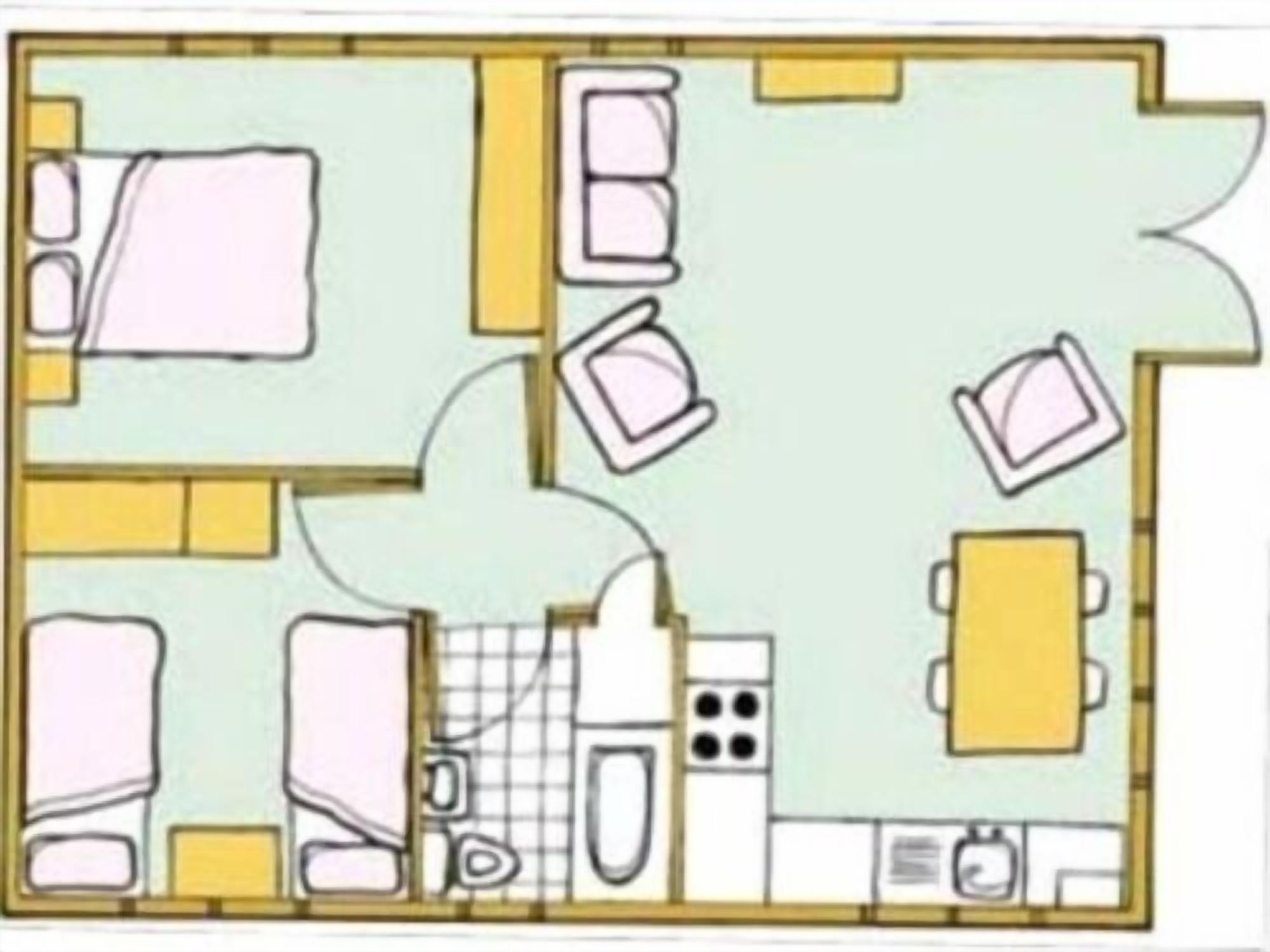 A hotel room layout with a bed, two bedside tables, a desk, a chair, a small bathroom with a toilet and sink, and a kitchenette area.