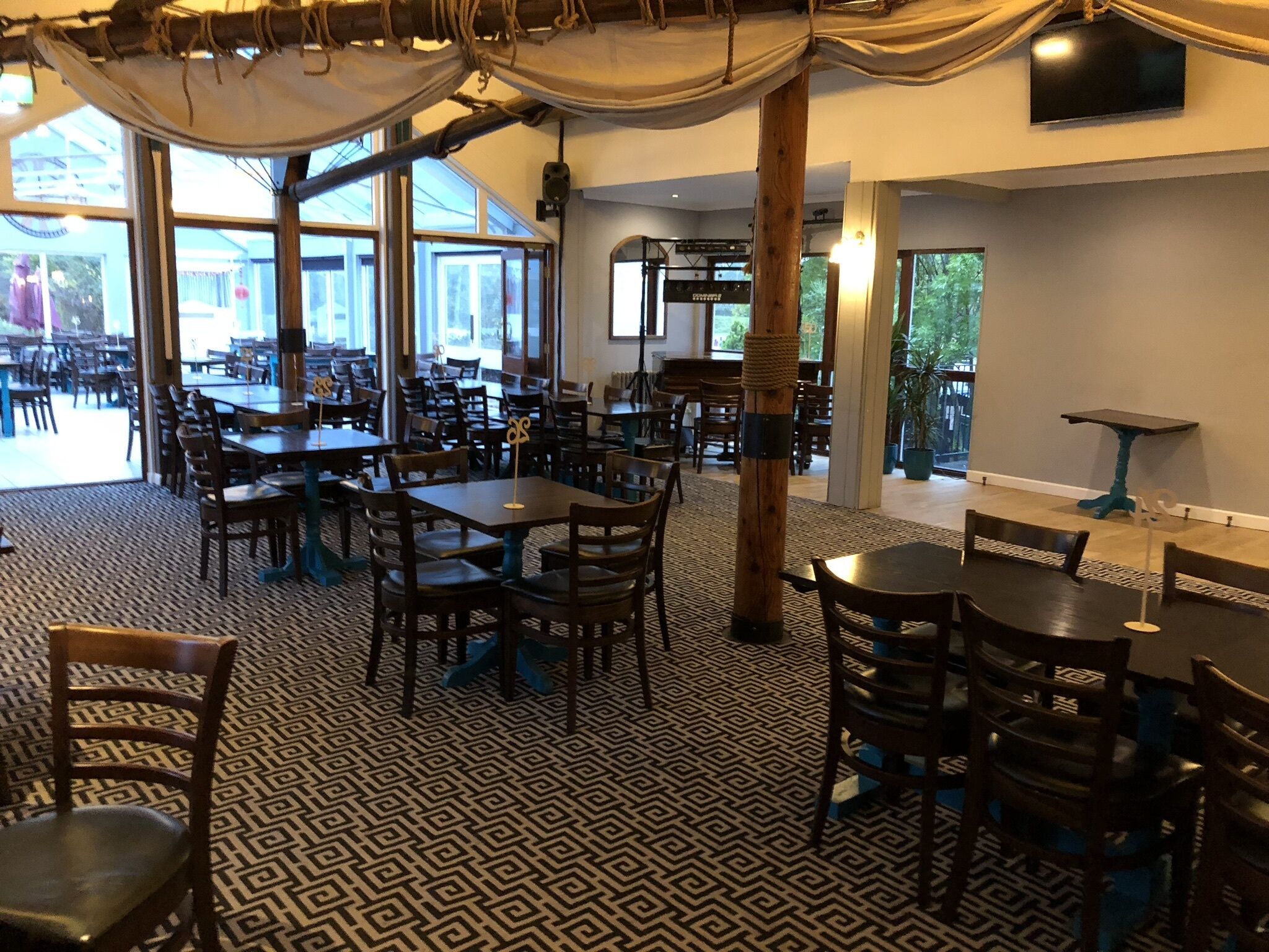 A spacious restaurant with multiple tables and chairs, large windows, and a patterned floor.