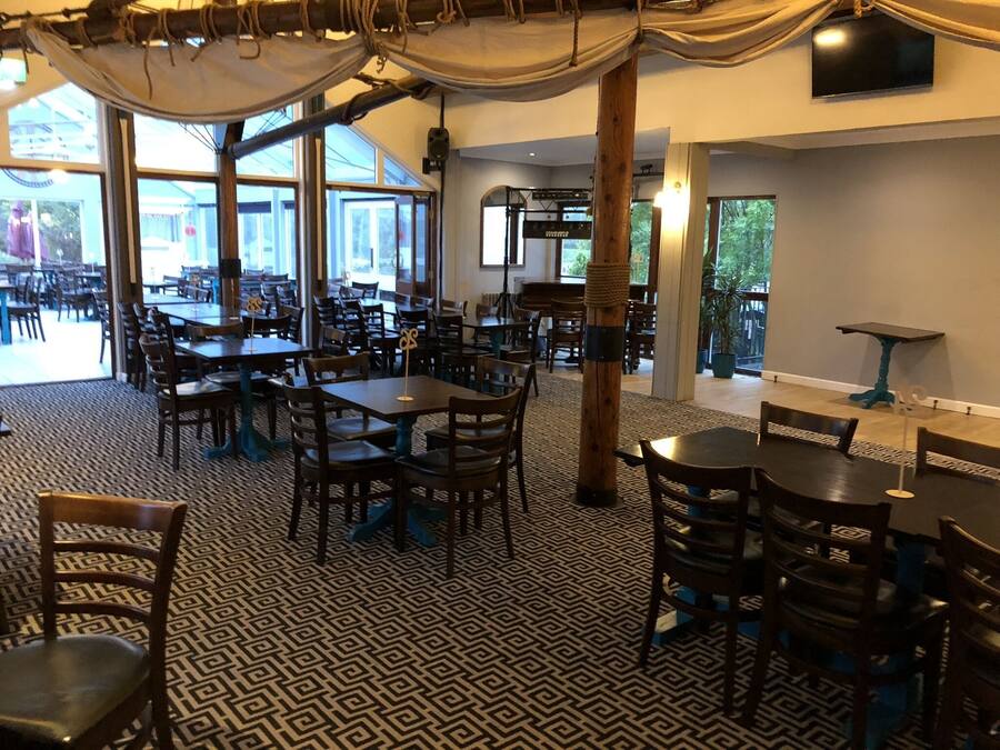 A spacious restaurant with multiple tables and chairs, large windows, and a patterned floor.