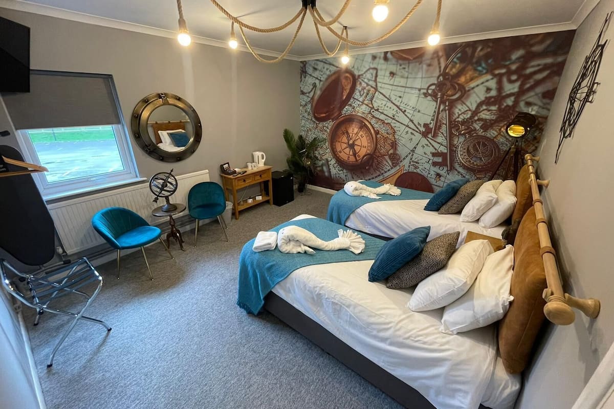 A hotel room with two beds, a desk, a chair, a map mural, and a window.