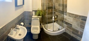 A bathroom with a toilet, bidet, sink, and a glass-enclosed shower.