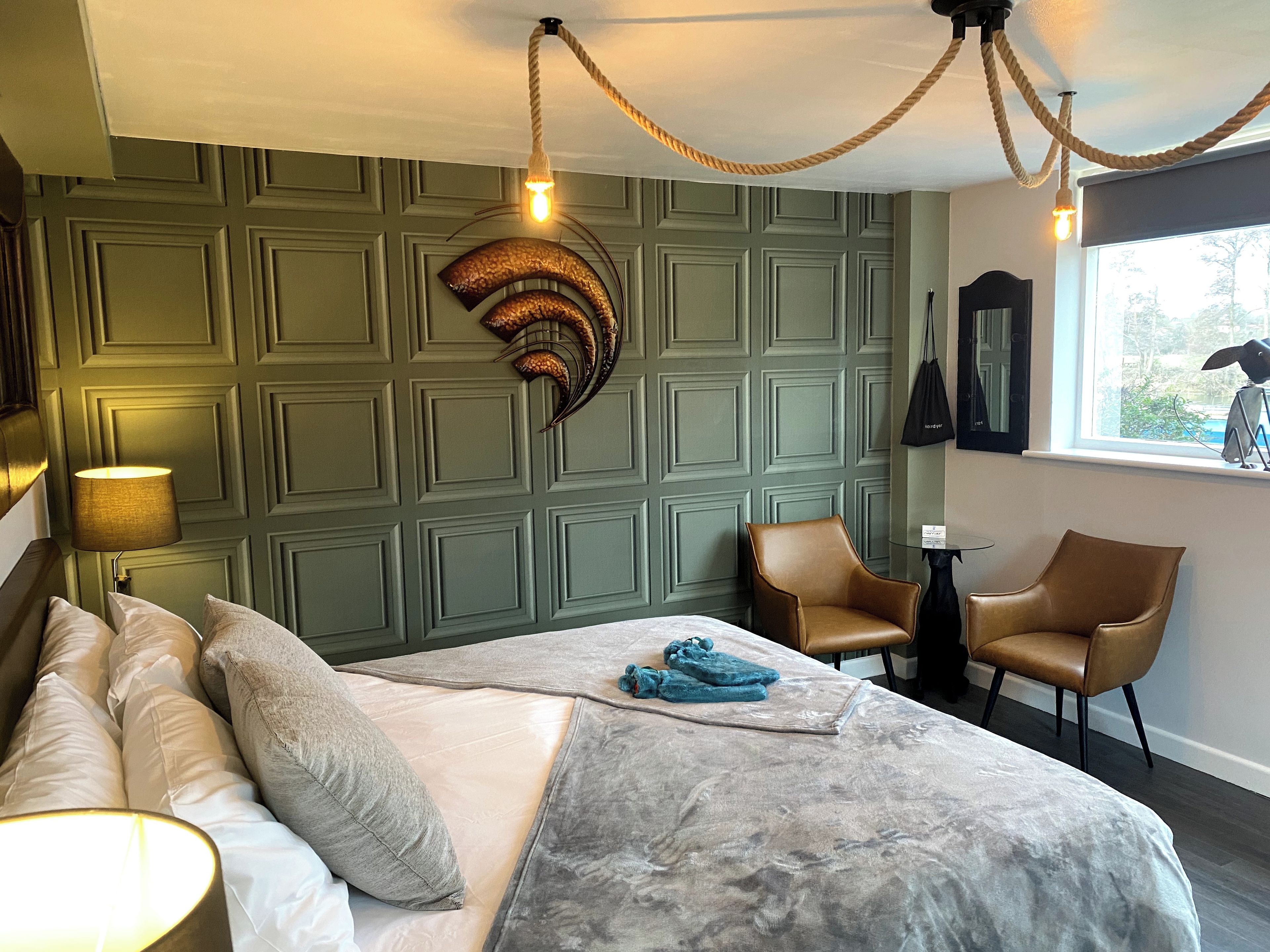 A bedroom with a bed, two chairs, a lamp, a decorative wall piece, and a window with a view.