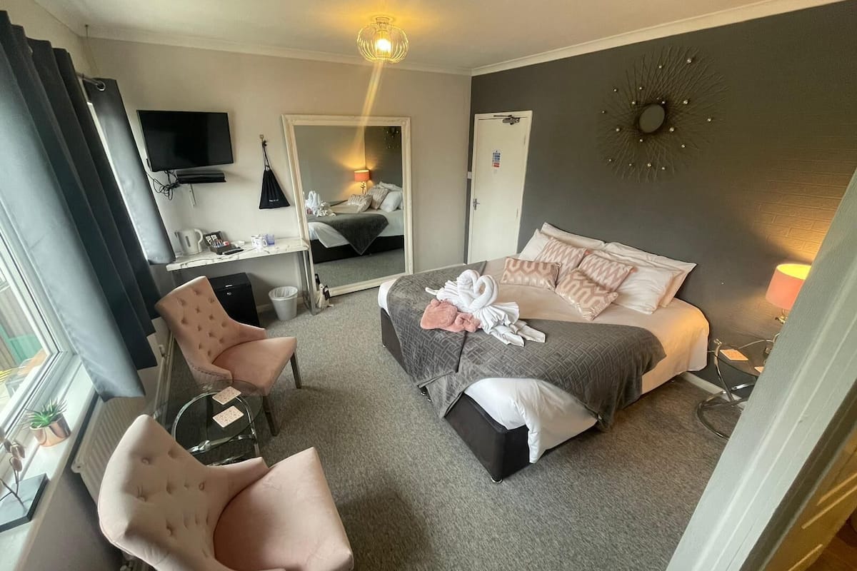 A hotel room with a bed, a desk, a chair, a TV, and a mirror.