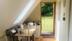 A small, cozy room with a sloped ceiling, wooden flooring, a dining table with chairs, a kitchenette, and a door leading to a balcony with a view of greenery. - Rosebank Bed & Breakfast (Etchingham)