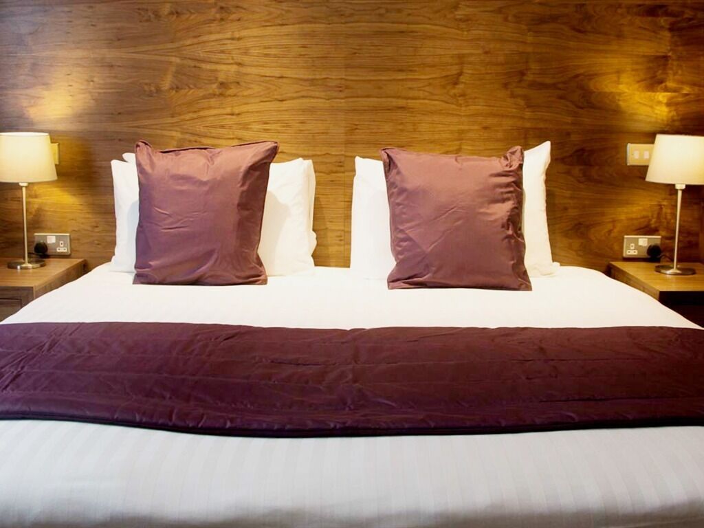 Una cama bien hecha con dos almohadas y un edredón oscuro.