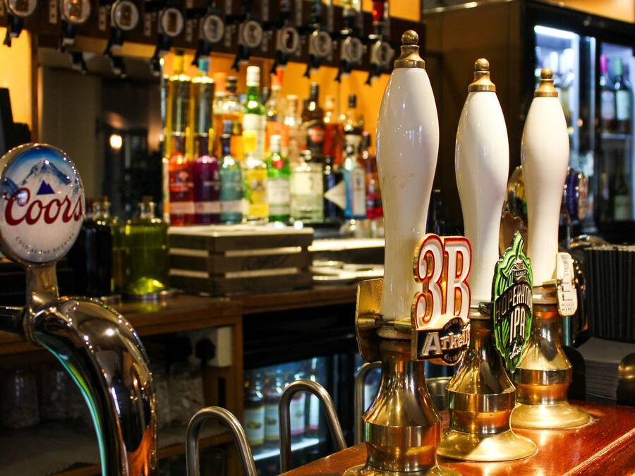 A bar with multiple beer taps, including Coors and 3B brands, and a variety of bottles in the background.