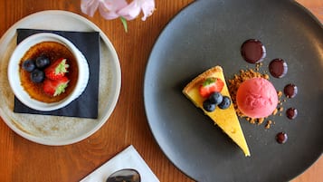 Un piatto da dessert con una fetta di cheesecake e gelato, una coppetta di crema brulée con fragole e mirtilli, e un cucchiaio su un tovagliolo.