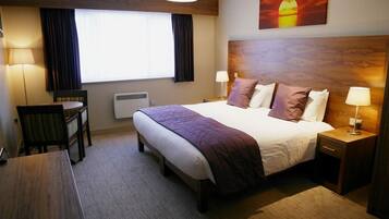A hotel room with a large bed, bedside tables, a desk, and a chair.