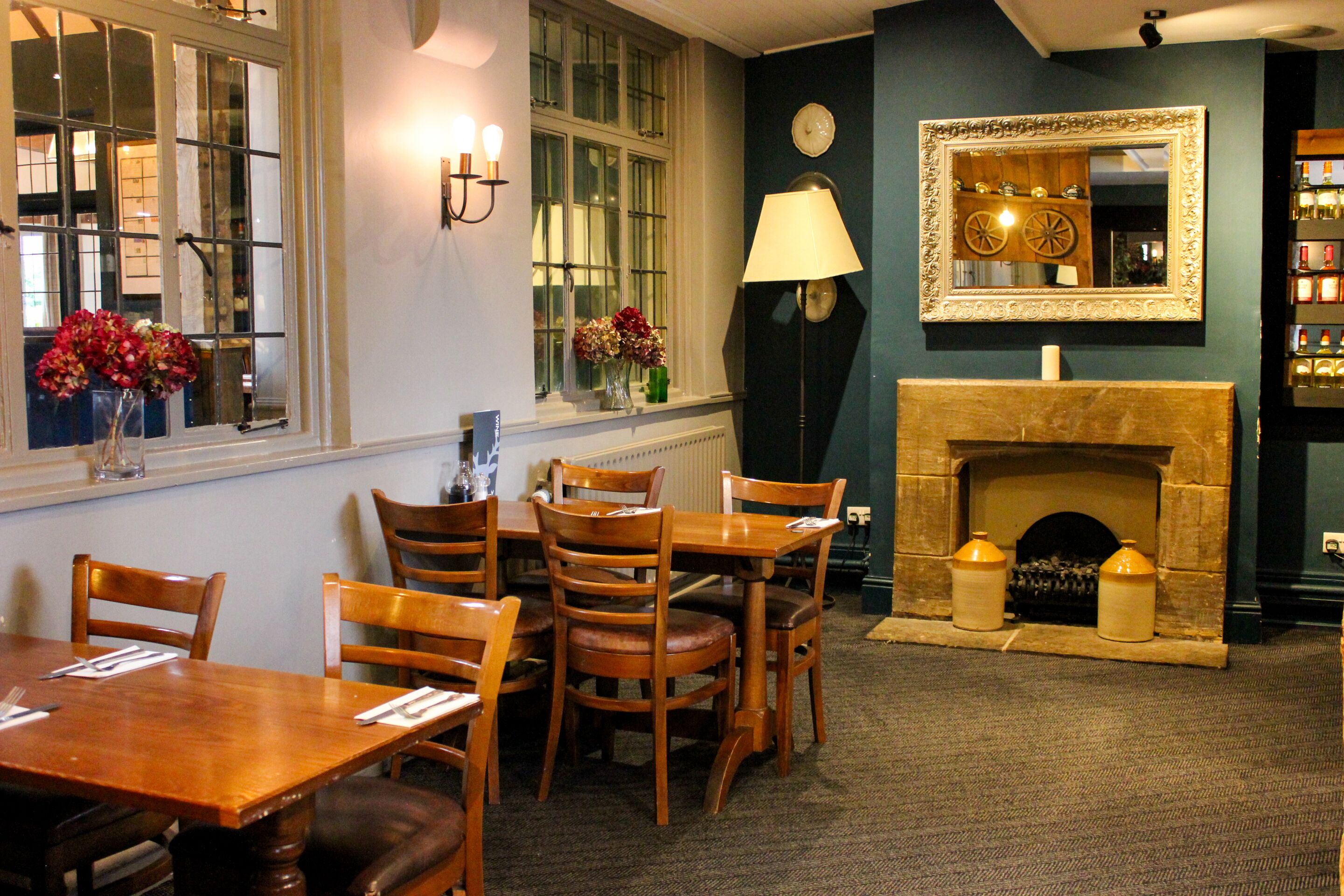 A dining area with a wooden table and chairs, a fireplace, and a window with flowers.