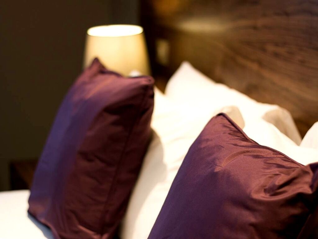 A bed with white bedding and two purple pillows.
