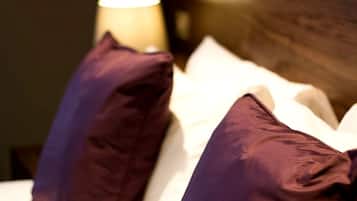 A bed with white bedding and two purple pillows.