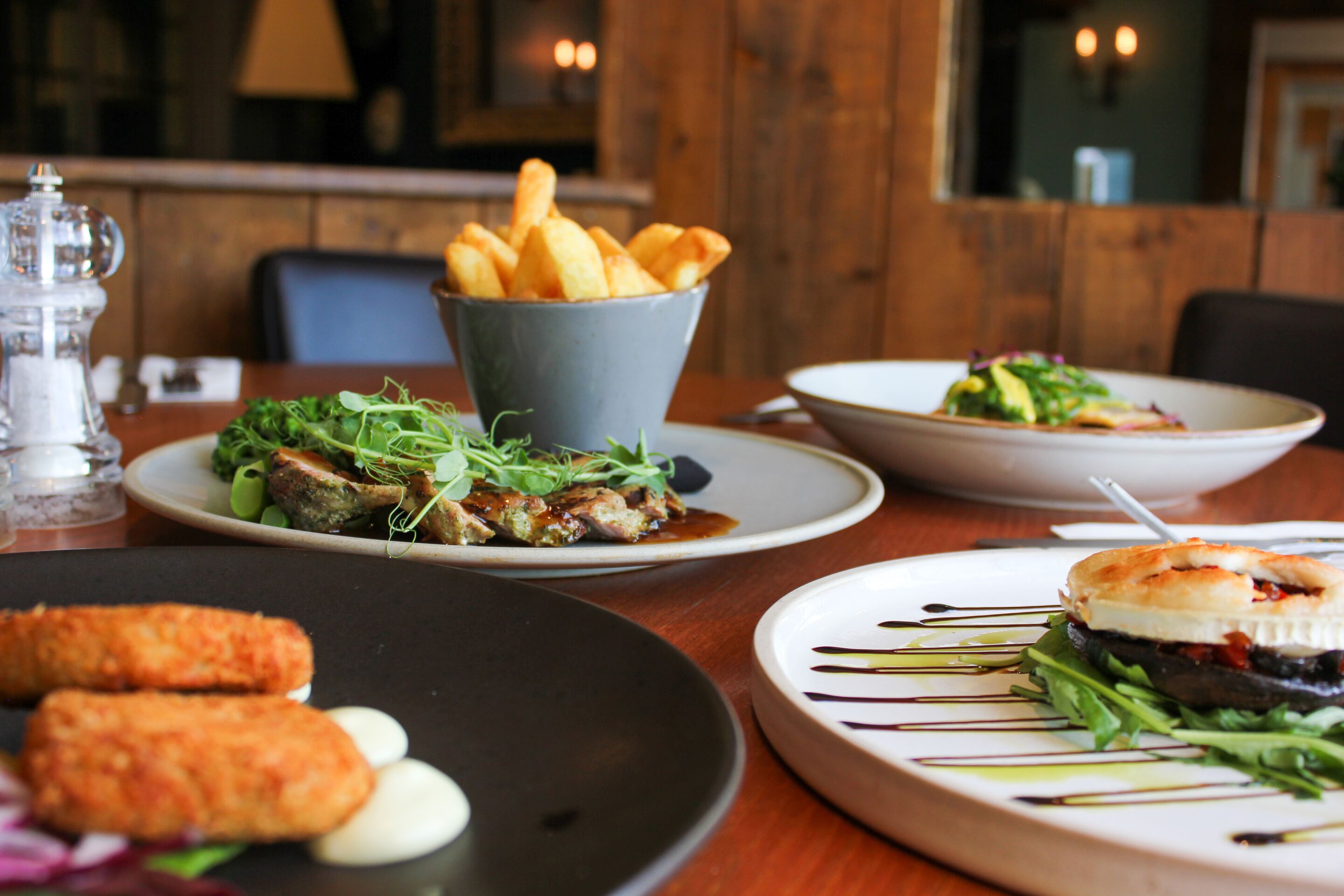 A restaurant table with various dishes, including a bowl of fries, a plate of greens, and a plate with a meat dish.