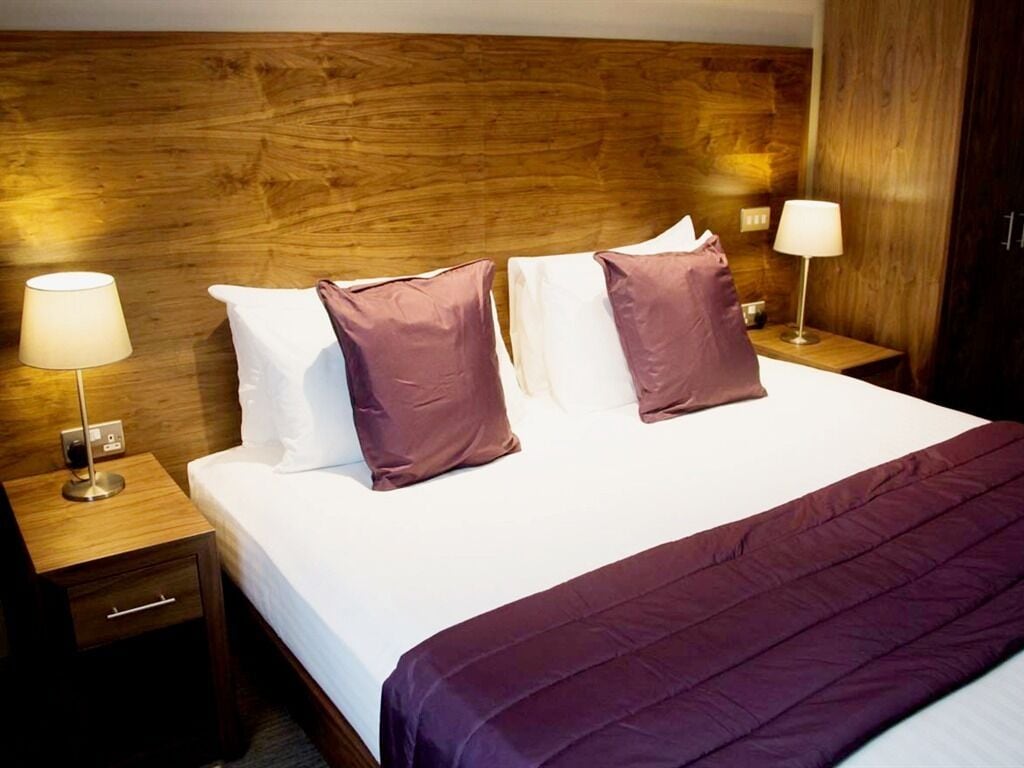 A neatly made bed with a wooden headboard, two bedside lamps, and a purple throw blanket.