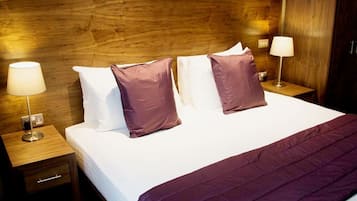 A neatly made bed with a wooden headboard, two bedside lamps, and a purple throw blanket.