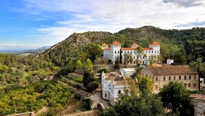 Un edificio grande e histórico con múltiples torres, rodeado de abundante vegetación y colinas.