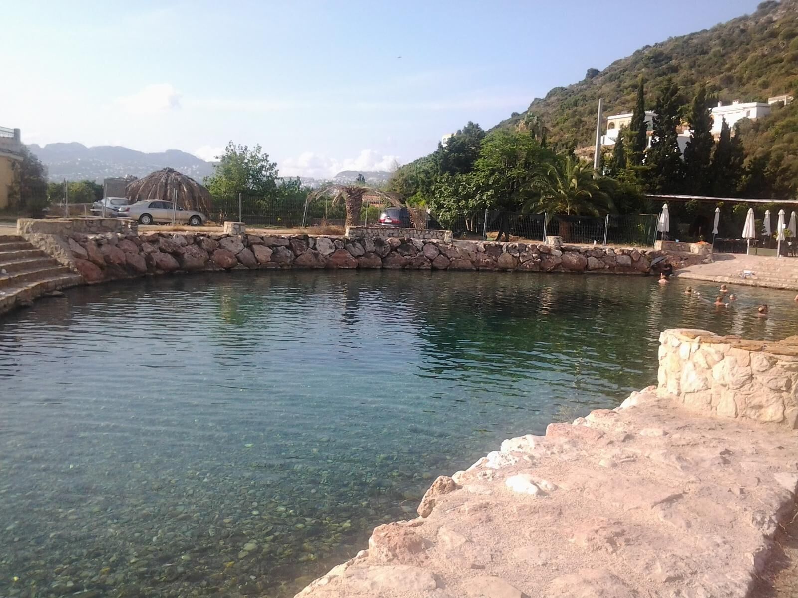 Une piscine aux eaux limpides, entourée de murs de pierre, avec un escalier en pierre menant à l’eau.