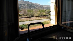 Vista desde una ventana a un paisaje montañoso, con una carretera y edificios a lo lejos.