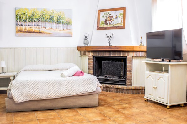 Un dormitorio con una cama, chimenea, televisor sobre un mueble bajo y obras de arte en las paredes.
