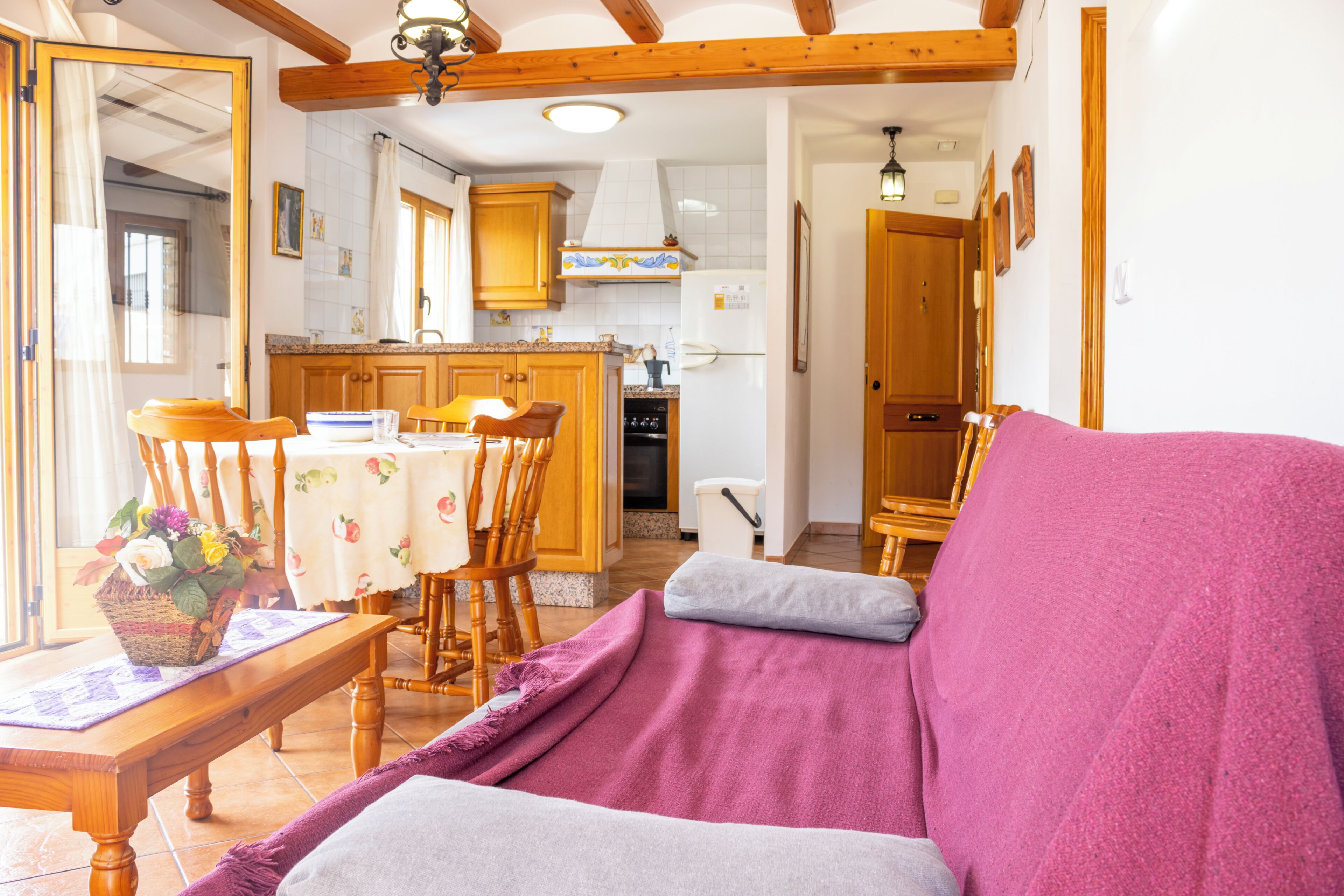 Un salon confortable avec un canapé, une table à manger et des chaises, ainsi qu’un coin cuisine doté de meubles en bois et d’un réfrigérateur.