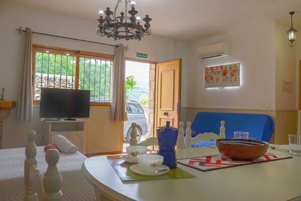 Habitación de hotel con televisor, una mesa de comedor con un bol y tazas, cafetera y vistas al exterior.