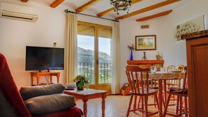Una sala de estar con televisor, un sofá, un comedor con sillas y una mesa, y un balcón con vistas.