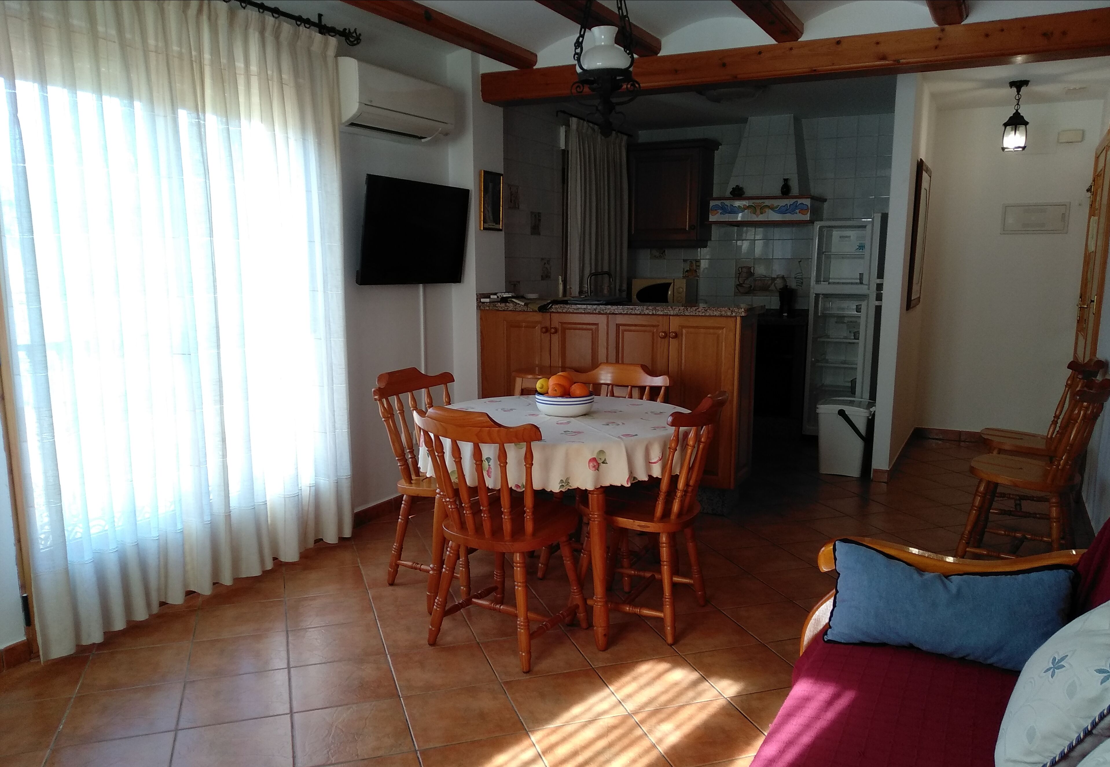 Un comedor con una mesa redonda y sillas, una cocina al fondo y una sala de estar con sofá.